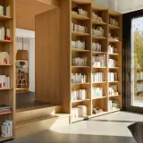 Jak zaplanować domową biblioteczkę według gatunków czy kolorów? Drewniane regały pełne książek, z widokiem na ogród.