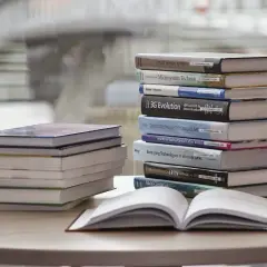 Stos książek i otwarta księga na stole. Czy warto brać udział w wyzwaniach czytelniczych typu 52 książki w rok?