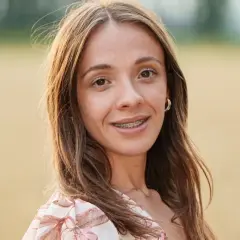 Wiktoria z Rolnik szuka żony, uśmiechnięta, z aparatem na zębach, w kwiecistej sukience, na tle pola.