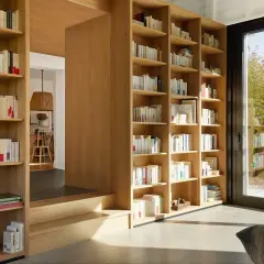 Jak zaplanować domową biblioteczkę według gatunków czy kolorów? Drewniane regały pełne książek, z widokiem na ogród.