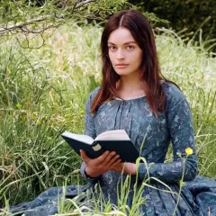 Młoda kobieta w sukni z epoki, czytająca książkę na łące, symbolizuje, jak ewoluowała postać kobieca w powieściach Jane Austen i sióstr Brontë.