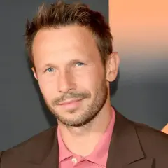Młody mężczyzna z niebieskimi oczami i krótkimi włosami, ubrany w brązową marynarkę i różową koszulę. Zastanawiasz się, ile lat ma Mateusz Banasiuk?