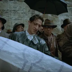 Mężczyźni w kapeluszach i płaszczach, pod parasolami, oglądają plany. Scena przypomina najciekawsze przykłady przemiany bohatera z dobrego w złego w literaturze.