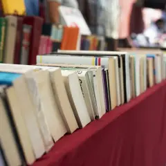 Rząd książek na czerwonym obrusie. Jak przygotować się do targów książki jako autor i czytelnik?