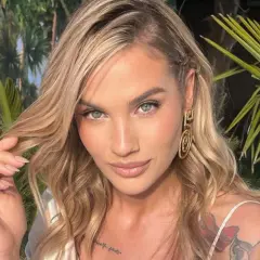 Karolina Gilon, z burzą blond włosów i tatuażami na ramieniu, pozuje na tle tropikalnej roślinności.