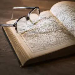 Okulary na otwartej księdze z mapą. Pomocne przy katalogowaniu źródeł i unikaniu błędów w researchu historycznym.