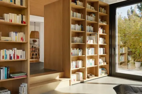 Jak zaplanować domową biblioteczkę według gatunków czy kolorów? Drewniane regały pełne książek, z widokiem na ogród.
