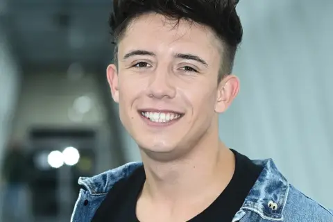 Uśmiechnięty Dawid Kwiatkowski w dżinsowej kurtce, jakby właśnie świętował dzień, kiedy urodził się Dawid Kwiatkowski.