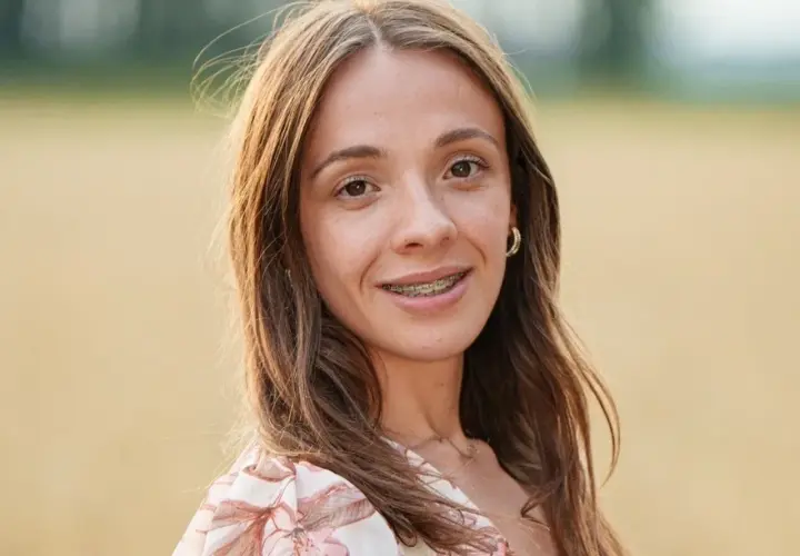 Wiktoria z Rolnik szuka żony, uśmiechnięta, z aparatem na zębach, w kwiecistej sukience, na tle pola.