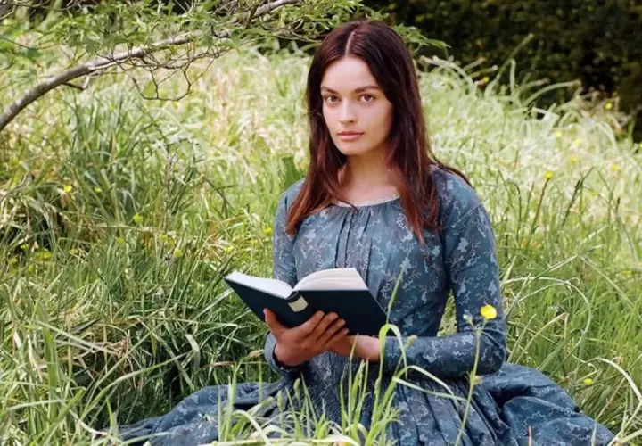 Młoda kobieta w sukni z epoki, czytająca książkę na łące, symbolizuje, jak ewoluowała postać kobieca w powieściach Jane Austen i sióstr Brontë.