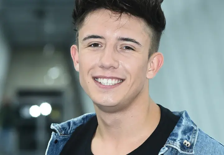 Uśmiechnięty Dawid Kwiatkowski w dżinsowej kurtce, jakby właśnie świętował dzień, kiedy urodził się Dawid Kwiatkowski.