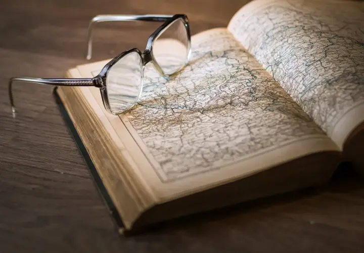 Okulary na otwartej księdze z mapą. Pomocne przy katalogowaniu źródeł i unikaniu błędów w researchu historycznym.