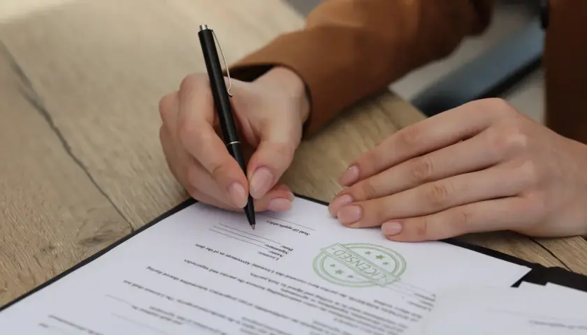 Ręka podpisuje dokument. Uważaj na zapisy, by uniknąć skutków podpisania niekorzystnej umowy wydawniczej.