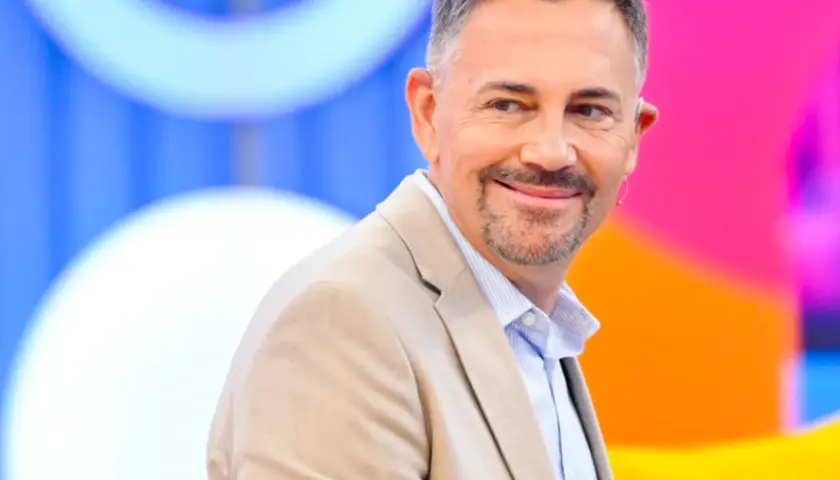 Krzysztof Ibisz, znany z programów telewizyjnych, uśmiecha się w beżowej marynarce. Jego wiek dodaje mu charyzmy.