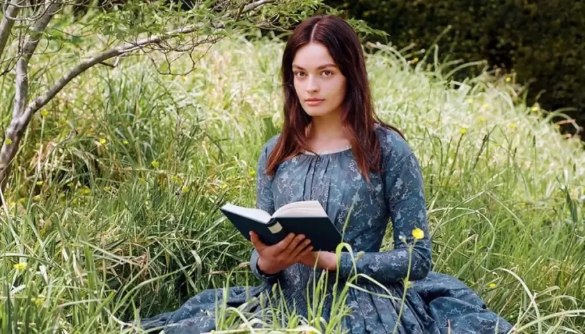 Młoda kobieta w sukni z epoki, czytająca książkę na łące, symbolizuje, jak ewoluowała postać kobieca w powieściach Jane Austen i sióstr Brontë.