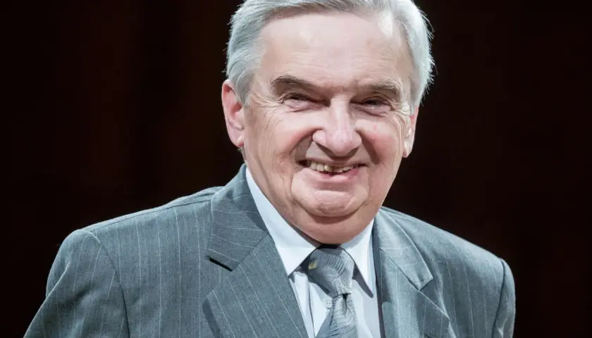 Uśmiechnięty starszy pan w szarym garniturze. Trudno zgadnąć, ile lat ma sznuk, ale wygląda na doświadczonego i życzliwego.