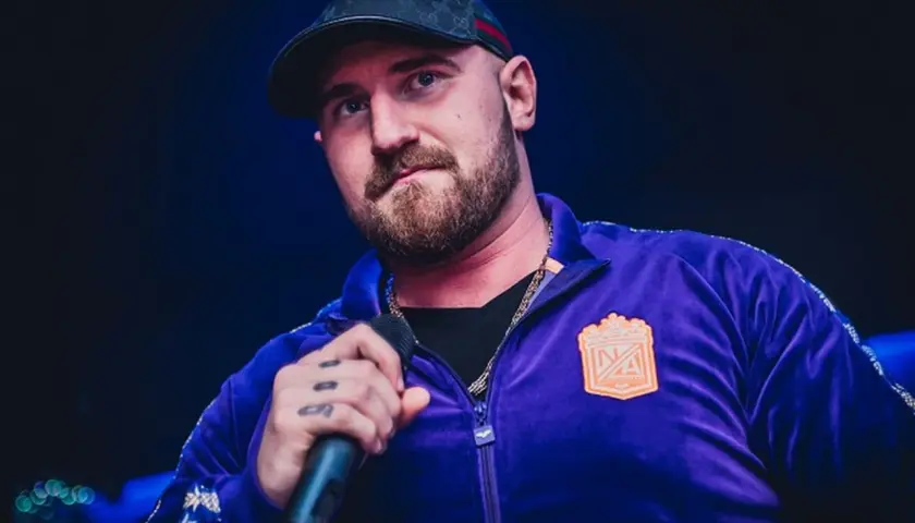 Kizo w fioletowej bluzie z kapturem i czapce, trzymający mikrofon. Fani zastanawiają się, ile wzrostu ma Kizo.