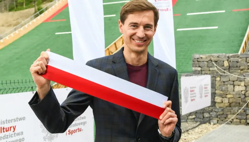 Uśmiechnięty mężczyzna trzyma biało-czerwoną wstęgę. Czy to symbol otwarcia obiektu, który ma ile lat stoch?