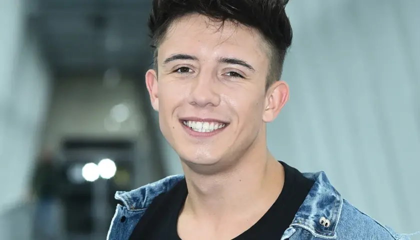 Uśmiechnięty Dawid Kwiatkowski w dżinsowej kurtce, jakby właśnie świętował dzień, kiedy urodził się Dawid Kwiatkowski.