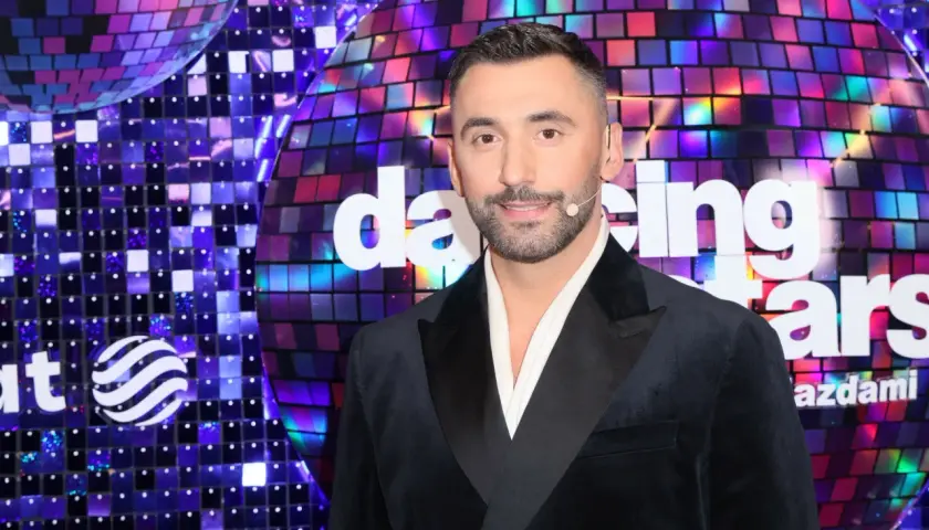 Maserak, ile lat ma? Uśmiechnięty mężczyzna w czarnym smokingu na tle błyszczącej sceny "Dancing with the Stars".