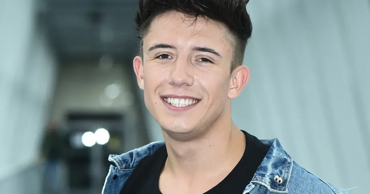 Uśmiechnięty Dawid Kwiatkowski w dżinsowej kurtce, jakby właśnie świętował dzień, kiedy urodził się Dawid Kwiatkowski.