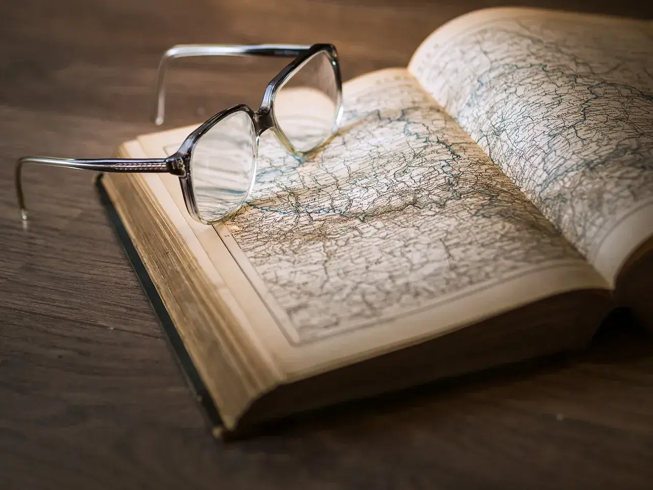 Okulary na otwartej księdze z mapą. Pomocne przy katalogowaniu źródeł i unikaniu błędów w researchu historycznym.