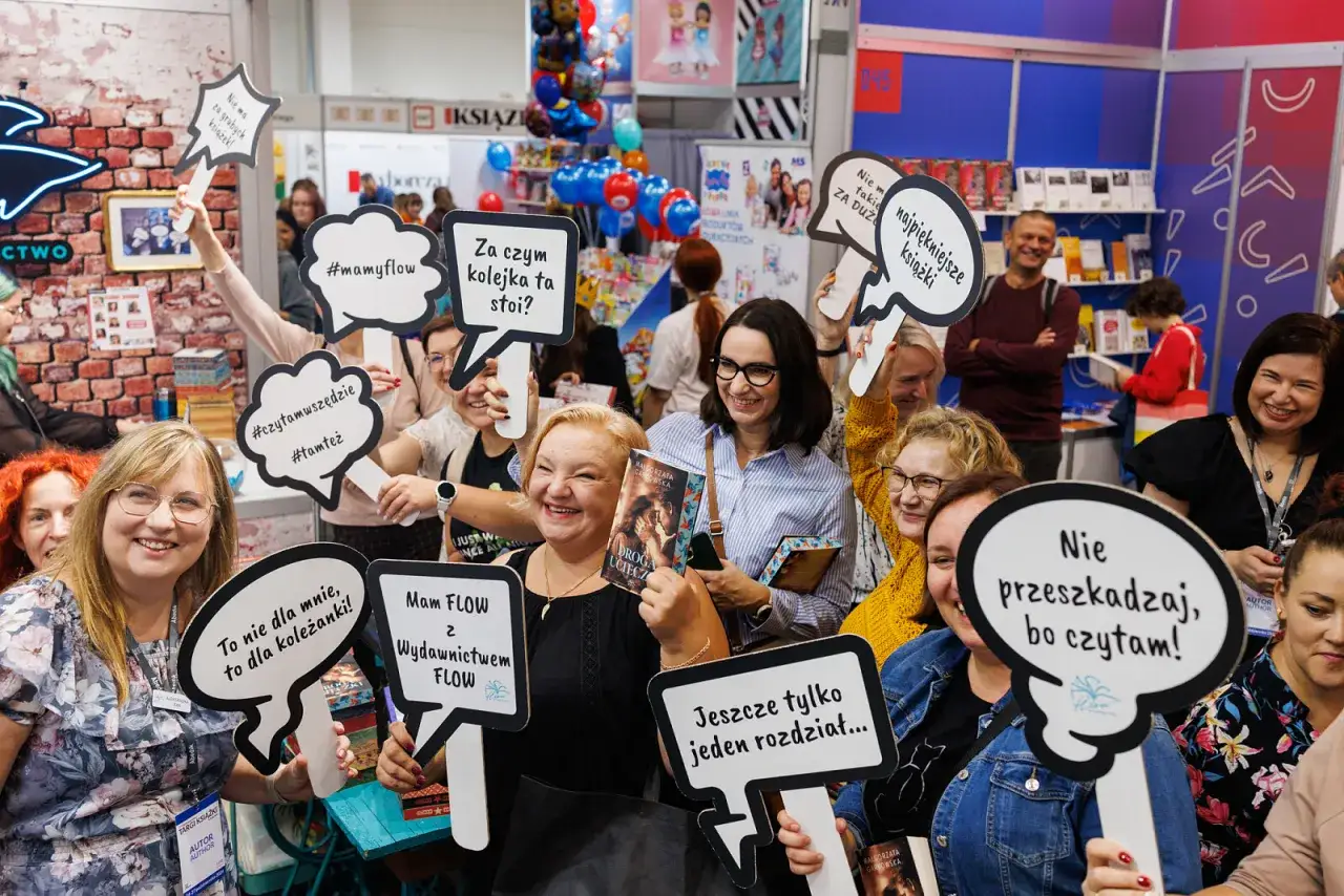 Uczestnicy na targach książki, gdzie odbywają się najważniejsze wydarzenia dla branży wydawniczej, trzymają tabliczki z napisami.